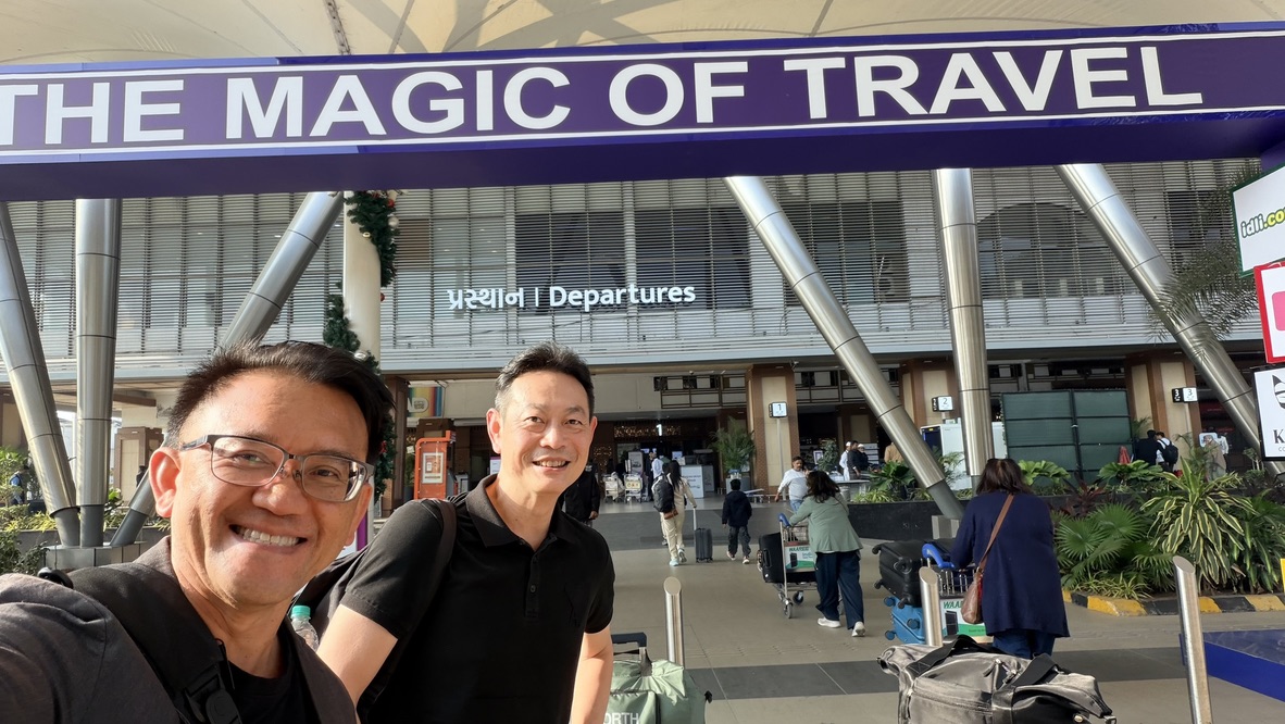 Two travellers with luggage outside an airport departures entrance, India.
