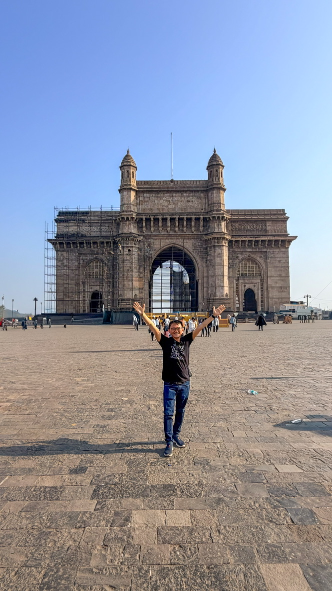 Traveller standing with raised arms before the Gateway of India, Mumbai, India.