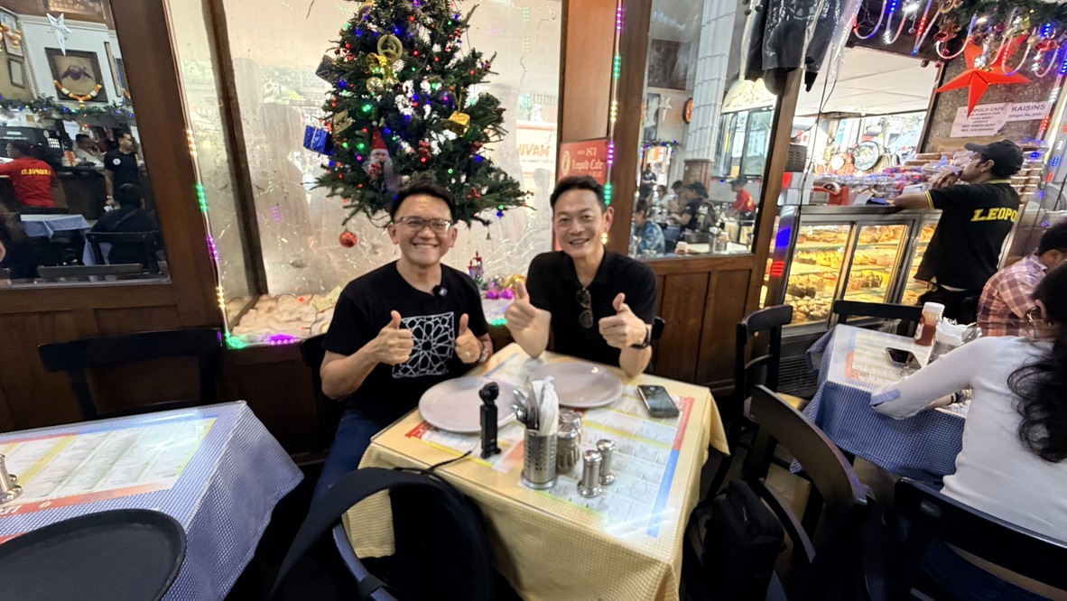 Two travellers seated beside a Christmas tree at Leopold Café, Mumbai, India.