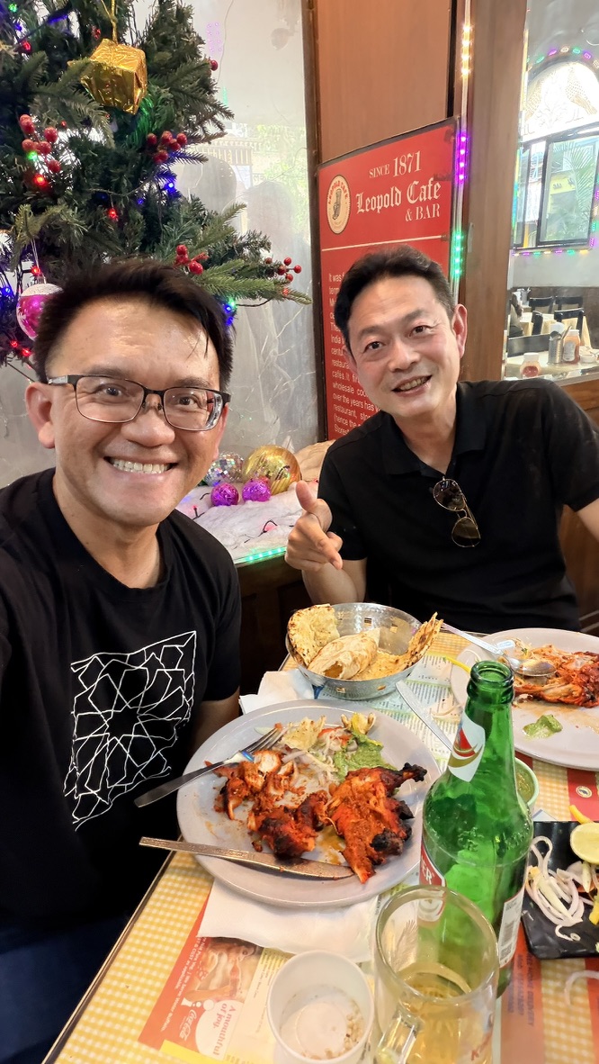 Two travellers smiling over lunch at Leopold Café, Mumbai, India.
