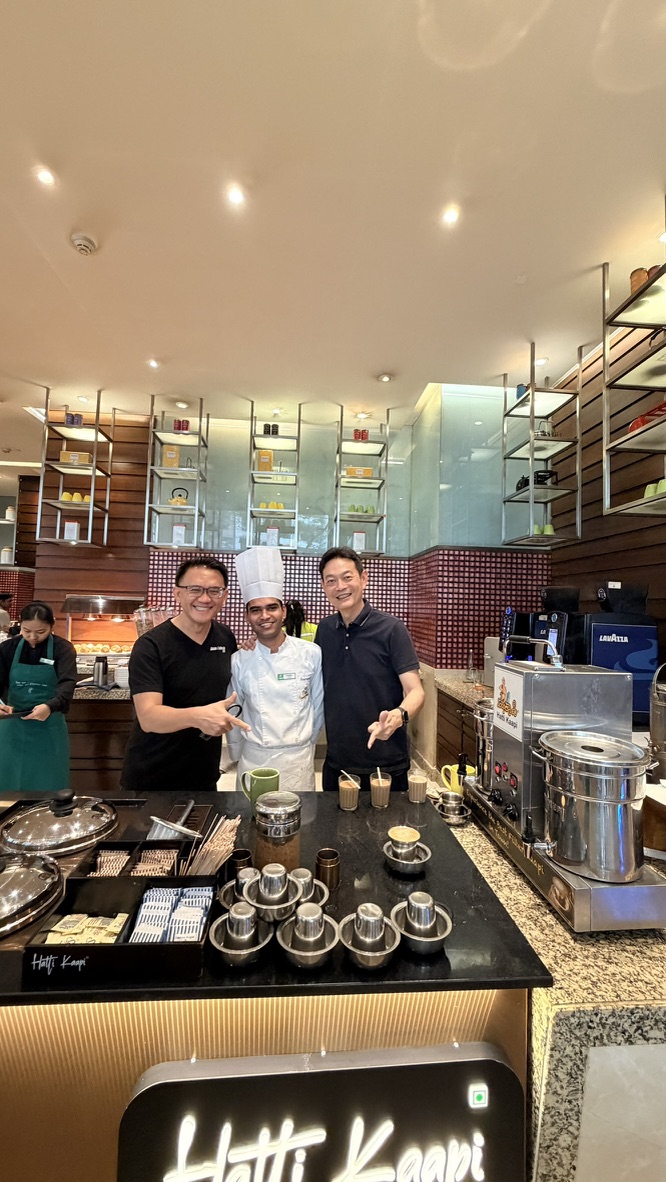 Two travellers with a chef at the Happy Kappi counter in a Mumbai hotel, India.