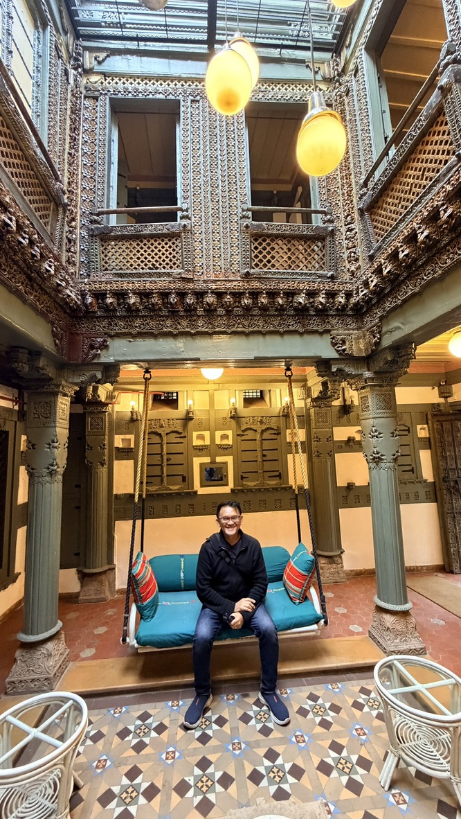 TOON seated on a traditional swing inside a richly carved haveli courtyard in Ahmedabad
