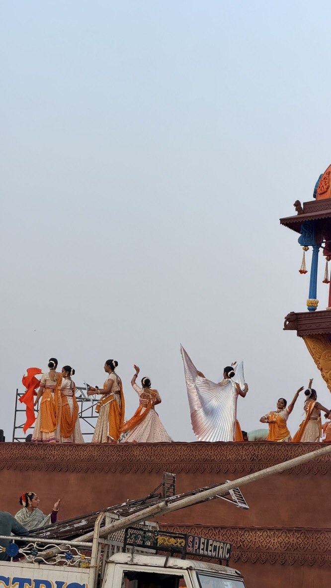 Performers in coordinated orange and white costumes dancing on a festival stage in Ahmedabad