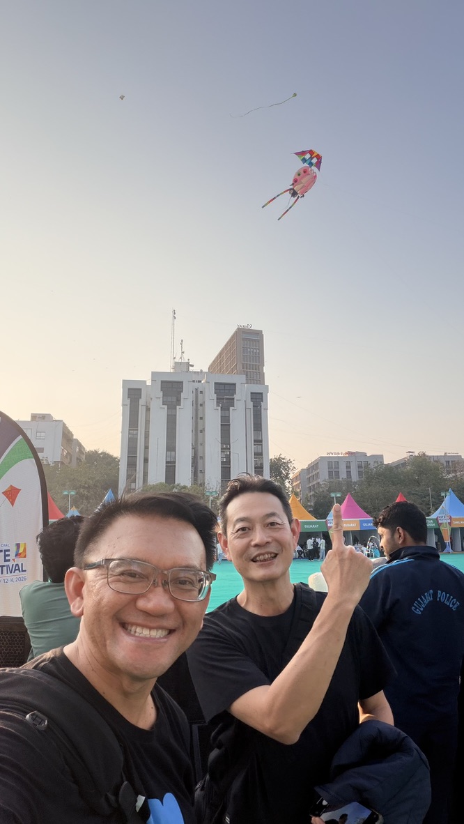 TOON and his travel companion pointing toward a colorful kite above the Ahmedabad festival grounds