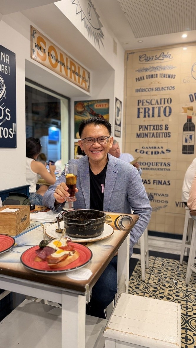 TOON holding a vermouth at the Casa Lola table with tapas in front of him