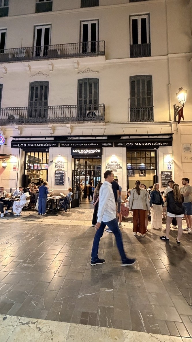 Los Marangos restaurant glowing onto a busy Málaga street at night