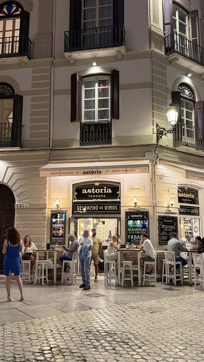 Astoria Taberna lit at a historic street corner in Málaga at night