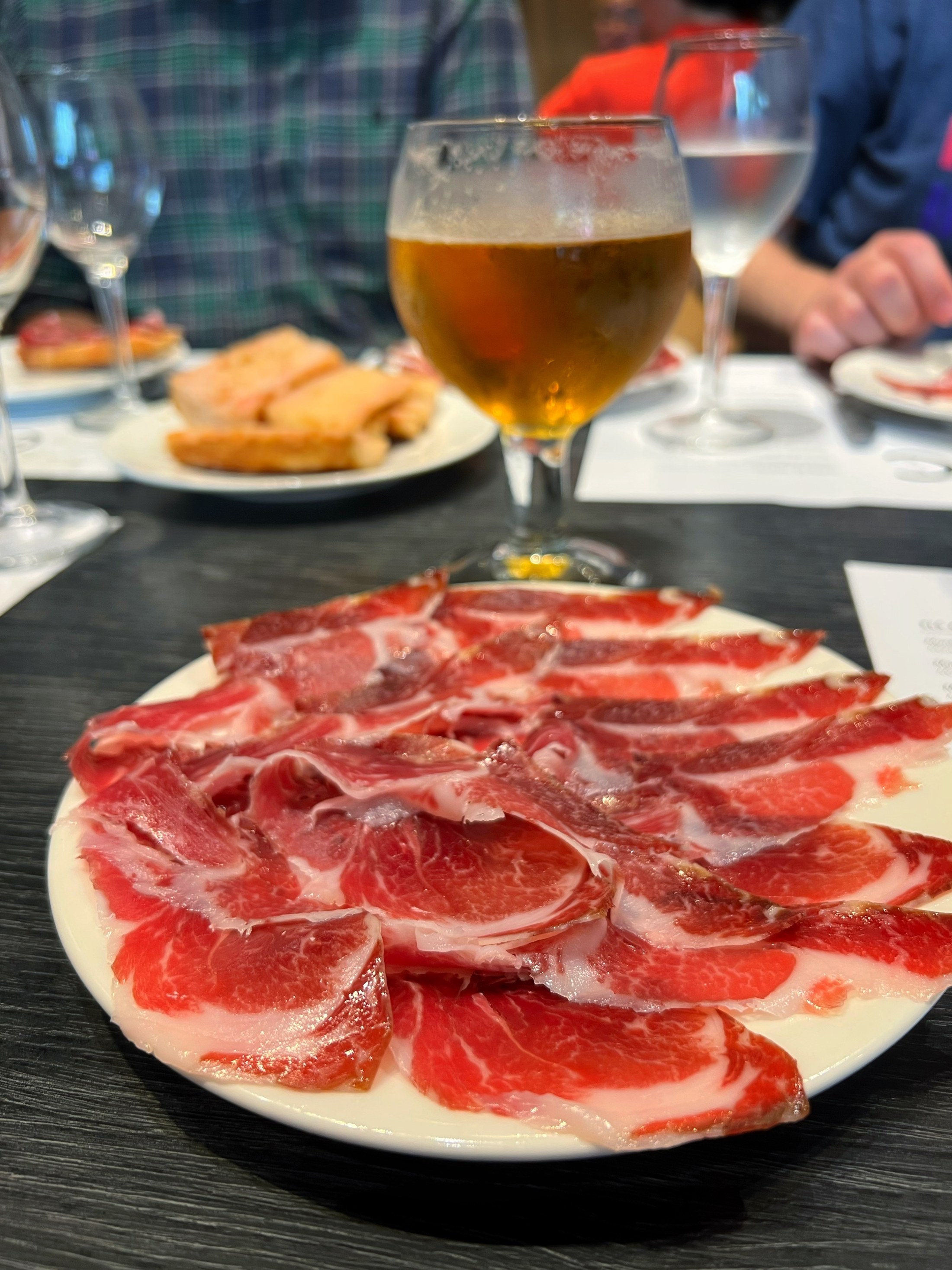 Thin slices of jamón ibérico served on a white plate with a beer nearby