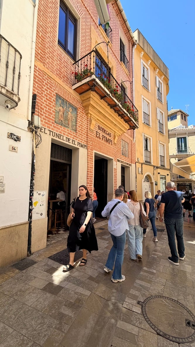 Pedestrians passing the red-brick El Pimpi building in Málaga